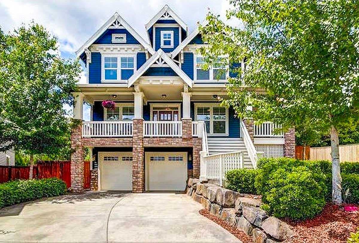 House plan exterior: three-story, blue siding, twin gables, covered porch, stone base, and double garage.