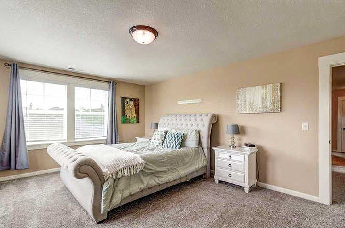 Bedroom with tufted headboard, large windows, and a nightstand with a lamp.