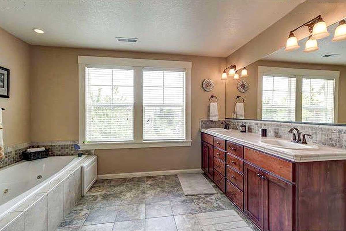 Bathroom with jetted tub, double vanity with dark wood cabinets, and two windows.