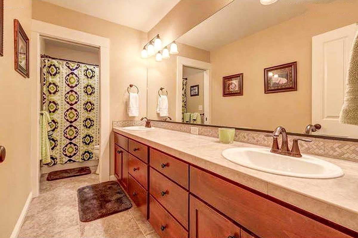 Bathroom with double vanity, wood cabinets, sinks, faucets, and a view into a shower with a patterned curtain.