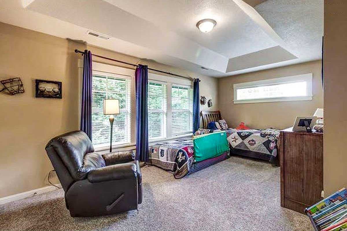 Bedroom with tray ceiling, two beds, recliner, and large windows with purple drapes.