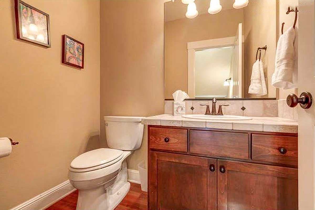 Powder room with wood vanity, tiled countertop, and toilet. Two framed pictures hang on the tan wall.