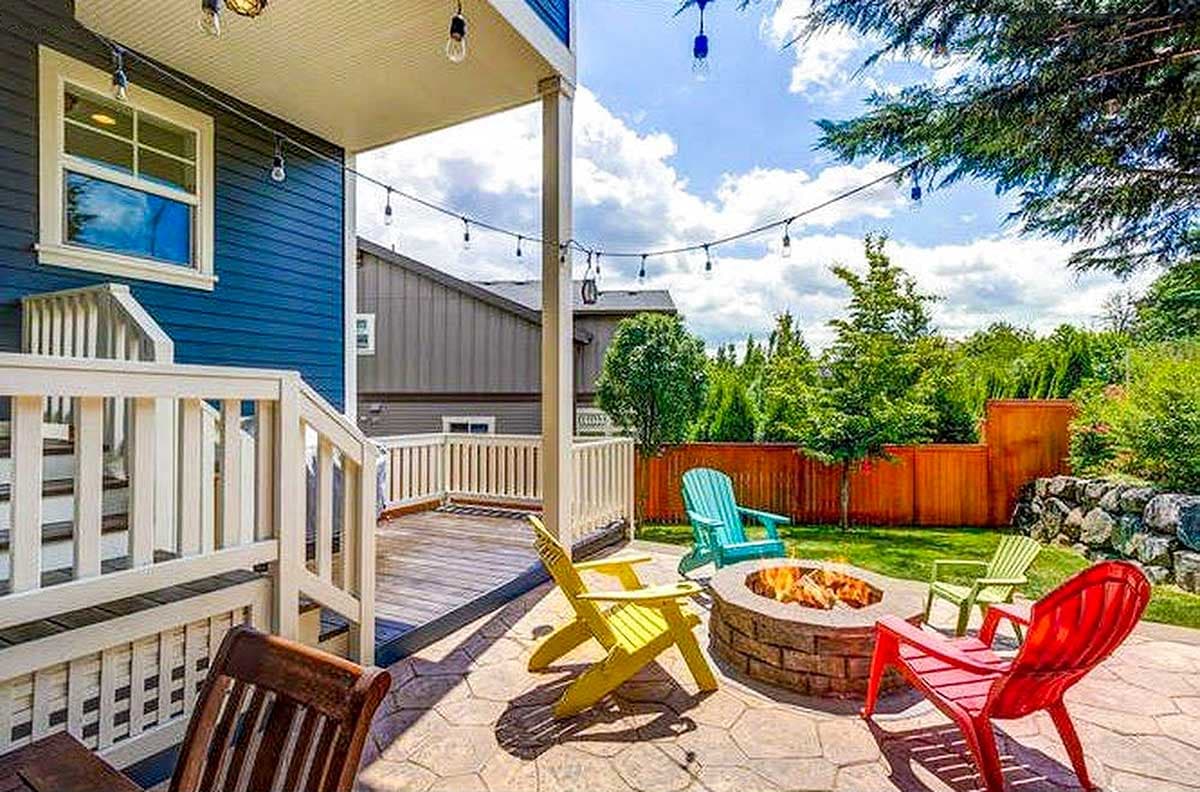 Outdoor living space with a multi-level deck, stone fire pit, Adirondack chairs, and string lights.