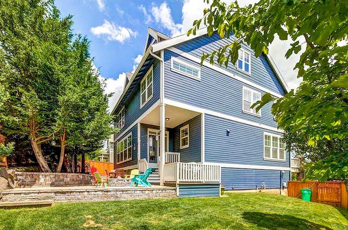 Three-story house plan exterior with blue siding, gables, dormers, and a covered front porch.