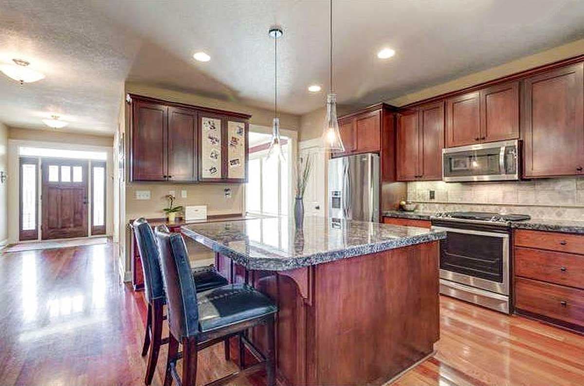 Kitchen with wood cabinets, granite island with seating, stainless steel appliances, and view of entryway.