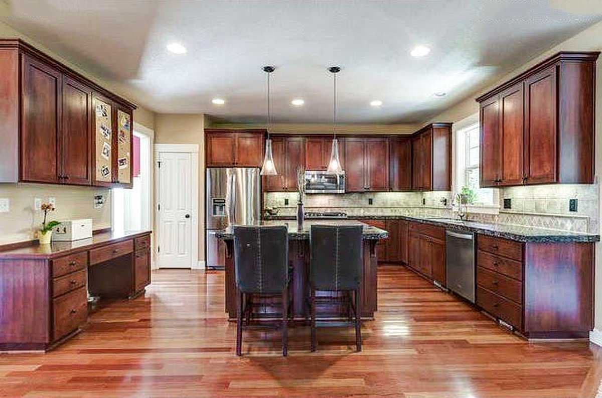 Kitchen interior with dark wood cabinetry, granite countertops, central island with seating, stainless steel appliances, and wood flooring.