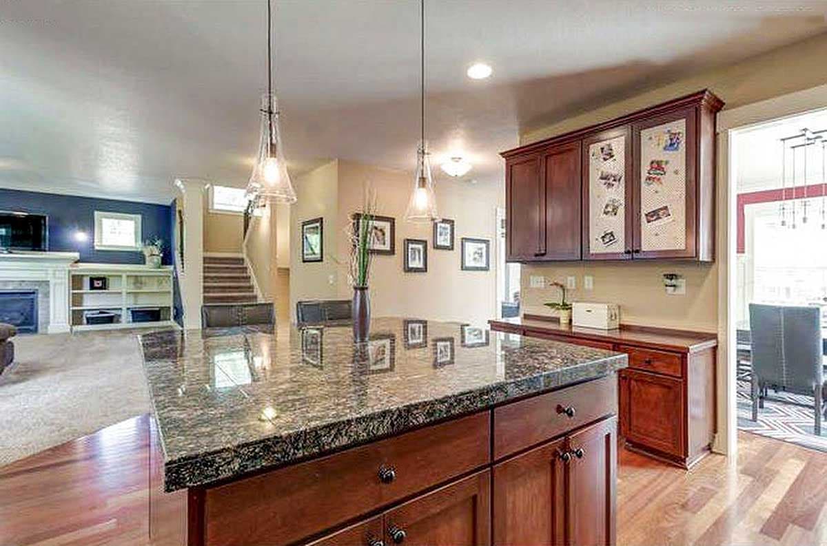 Kitchen island with granite countertop, dark wood cabinets, pendant lights, and view of living room with fireplace.