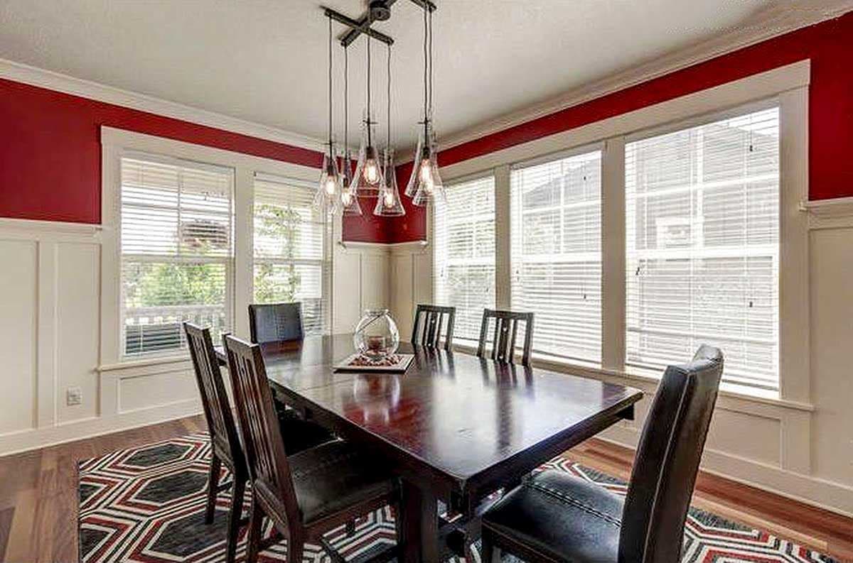 Dining room with wood table, chairs, multi-light pendant, wainscoting, and large windows.