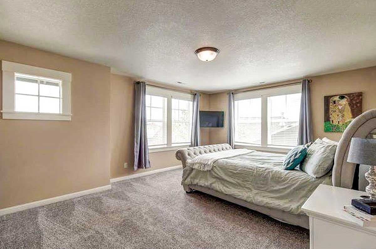 Bedroom with tufted headboard, three large windows, and a small television mounted on the wall.