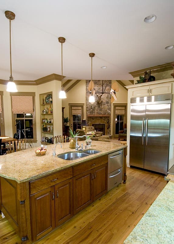 Kitchen interior with large island, granite countertops, stainless steel appliances, and a stone fireplace.