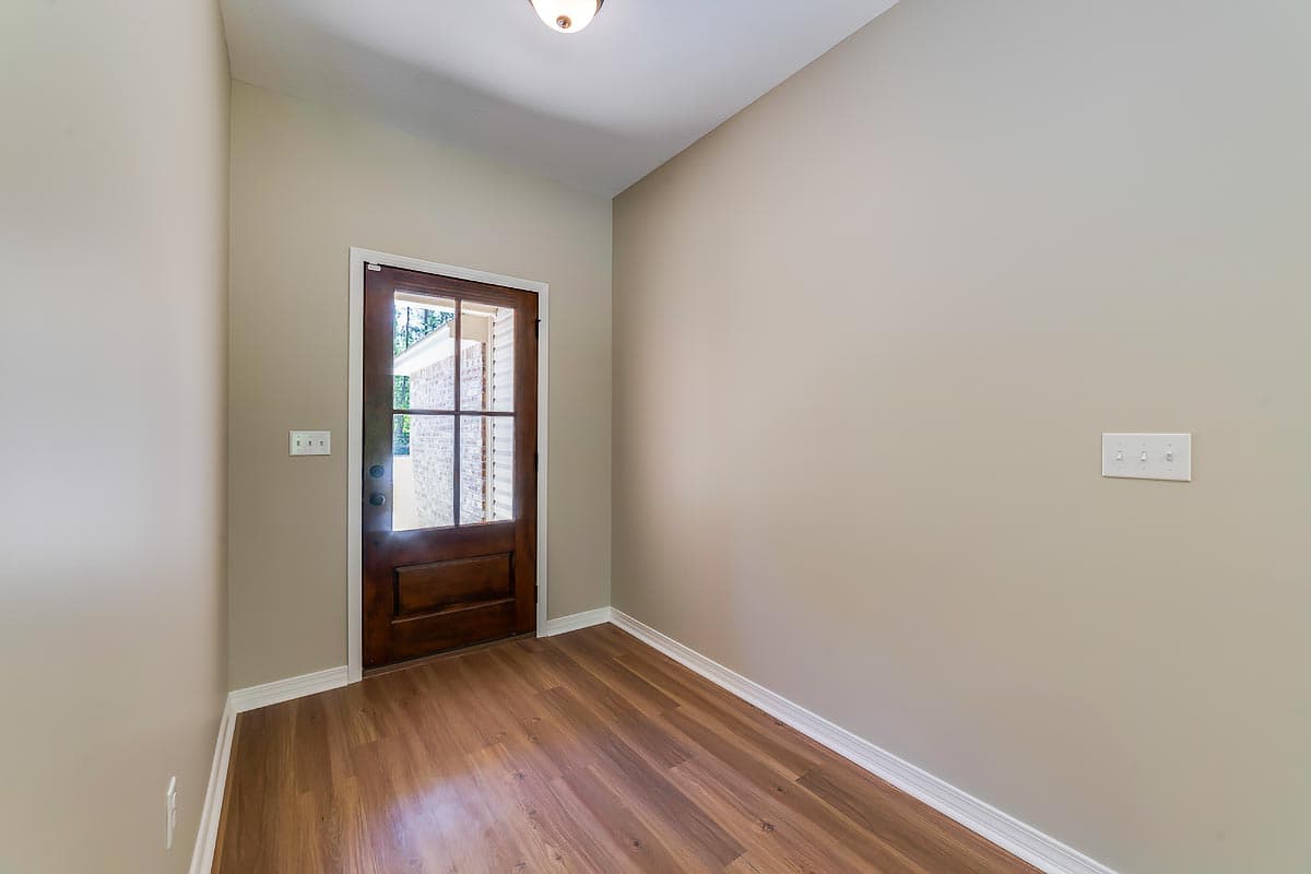 Interior view of an entryway with a dark wood door featuring a glass pane, laminate flooring, and neutral walls.