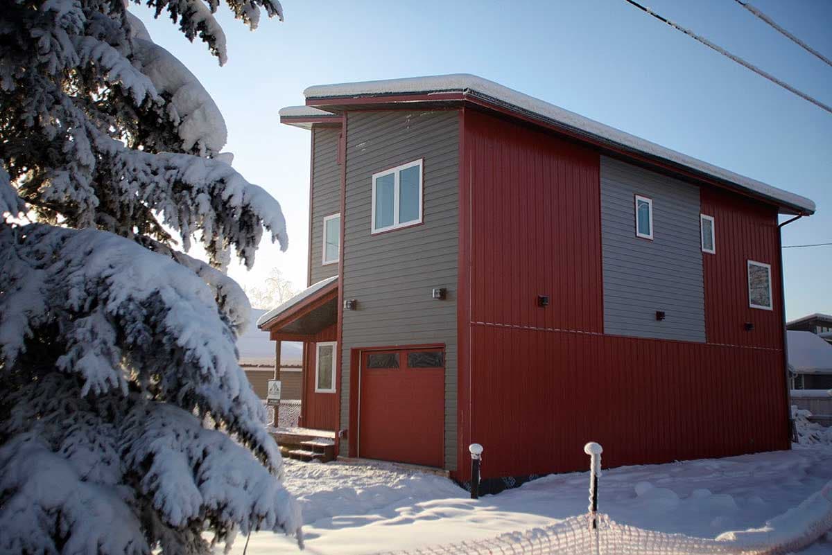 House plan exterior: two-story modern home with red and gray siding, attached garage, and covered entryway in snow.
