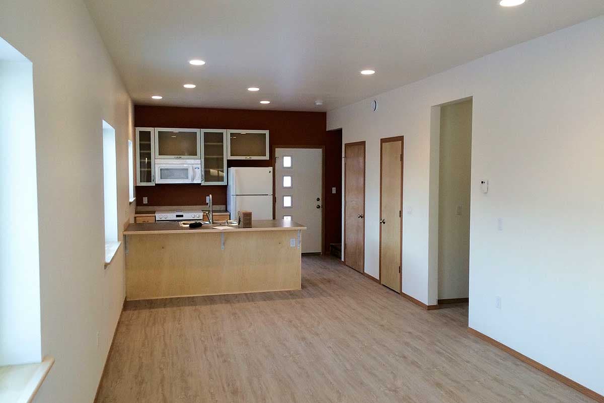 Interior view showing a kitchen with a central island, white cabinets, and appliances, opening to a hallway with two doors.