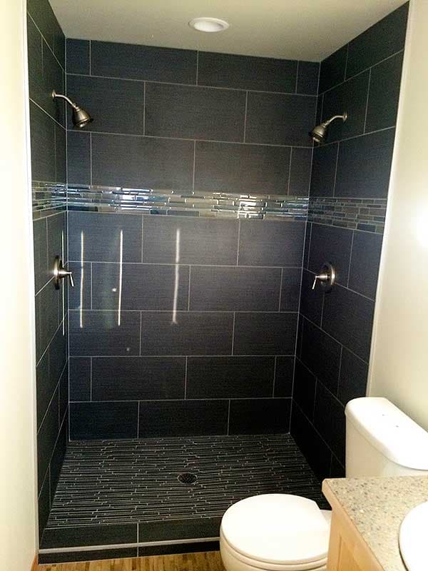 Tiled shower with dual shower heads, decorative mosaic band, and linear tile floor. Toilet visible.