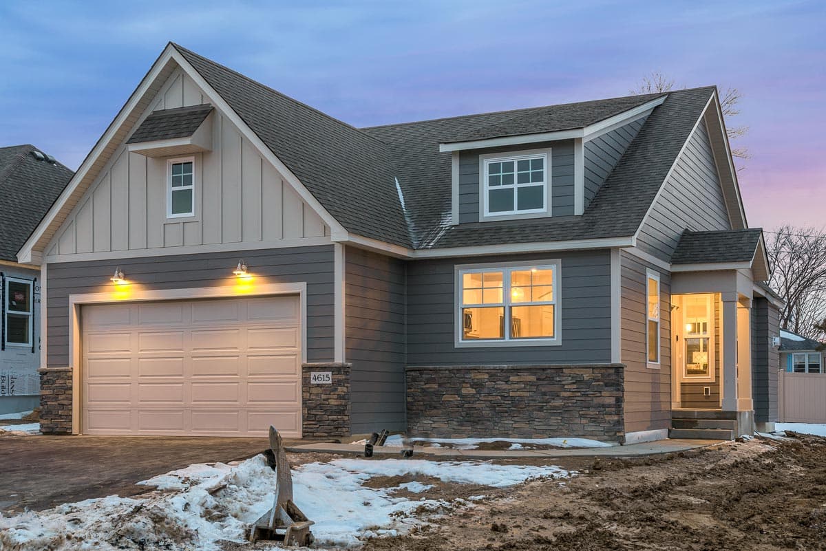 House plan exterior shows a two-story home with a gable roof, board and batten siding, stone base, and attached garage.