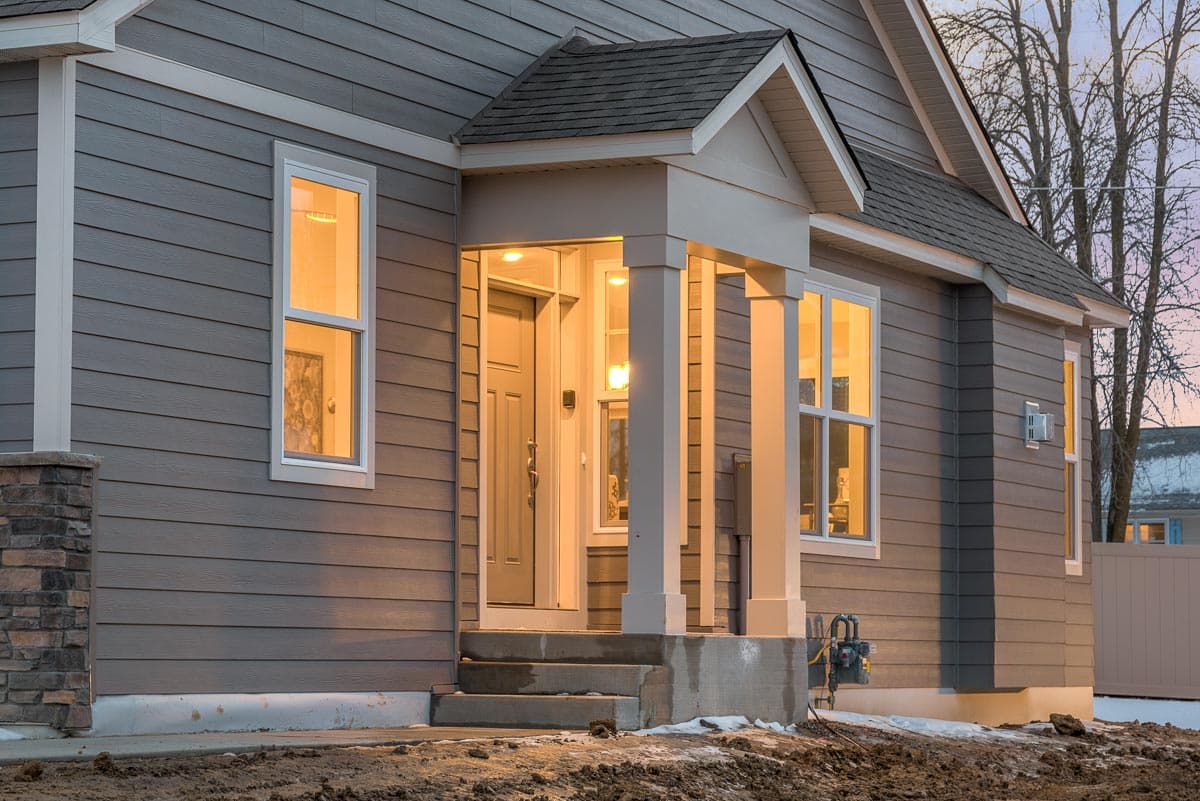 House plan exterior: Modern Farmhouse style, single-story with covered front porch, double gabled roof, and stone accent pillar.