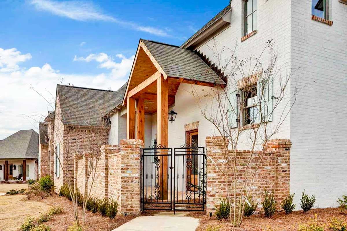 House plan exterior featuring a covered entry with wooden beams, brick wall, and ornate metal gate.