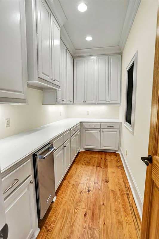 Pantry interior with light gray cabinets, white countertops, stainless steel dishwasher, and wooden floor.