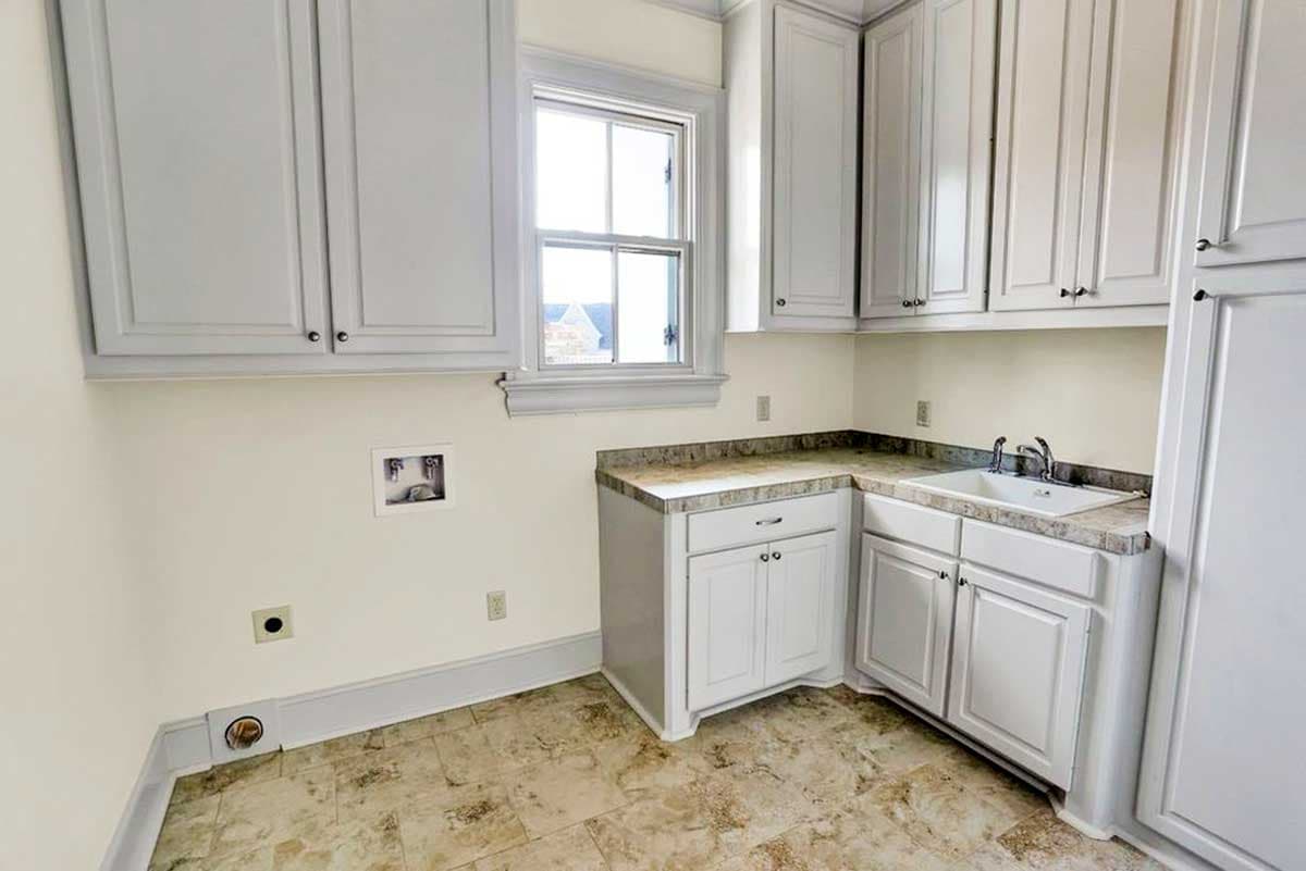 Laundry room interior with white cabinets, sink, countertop, window, and washer/dryer hookups.