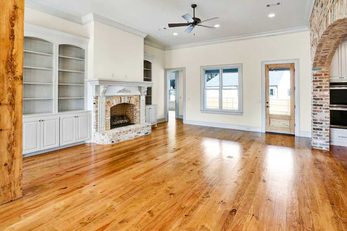 Living room interior with built-in bookshelves, fireplace, wood floor, and arched brick entry to kitchen.