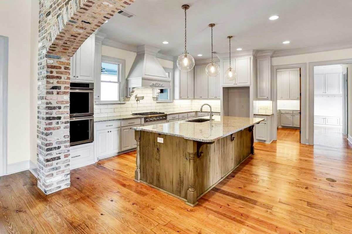 Kitchen with rustic wood island, double ovens, subway tile backsplash, and arched brick entry.