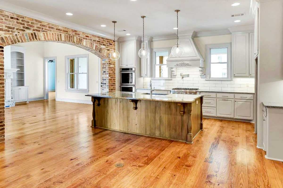 Kitchen with large wooden island, brick archway, white cabinetry, subway tile backsplash, and stainless steel appliances.
