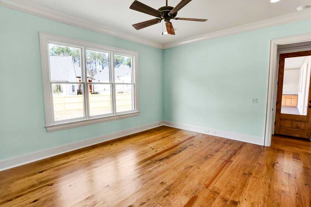 Interior room with light blue walls, hardwood floors, large multi-pane window, and ceiling fan. Doorway to another room.