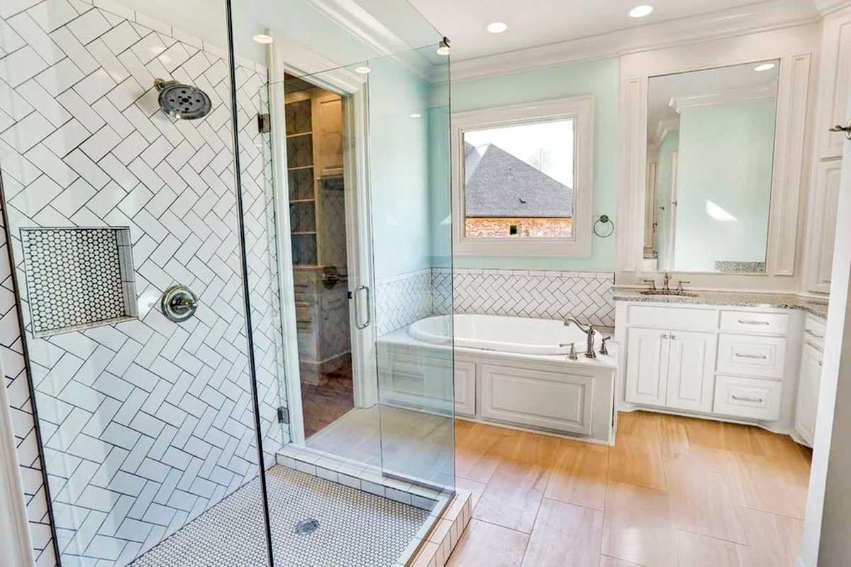 Bathroom with herringbone tile shower, soaking tub, dual vanity with granite countertops, and wood-look tile flooring.