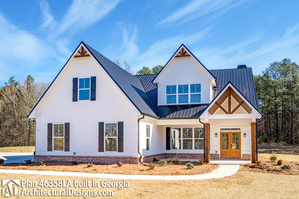 Modern farmhouse house plan exterior with white siding, metal roof, prominent gables, and wood-trimmed entryway.