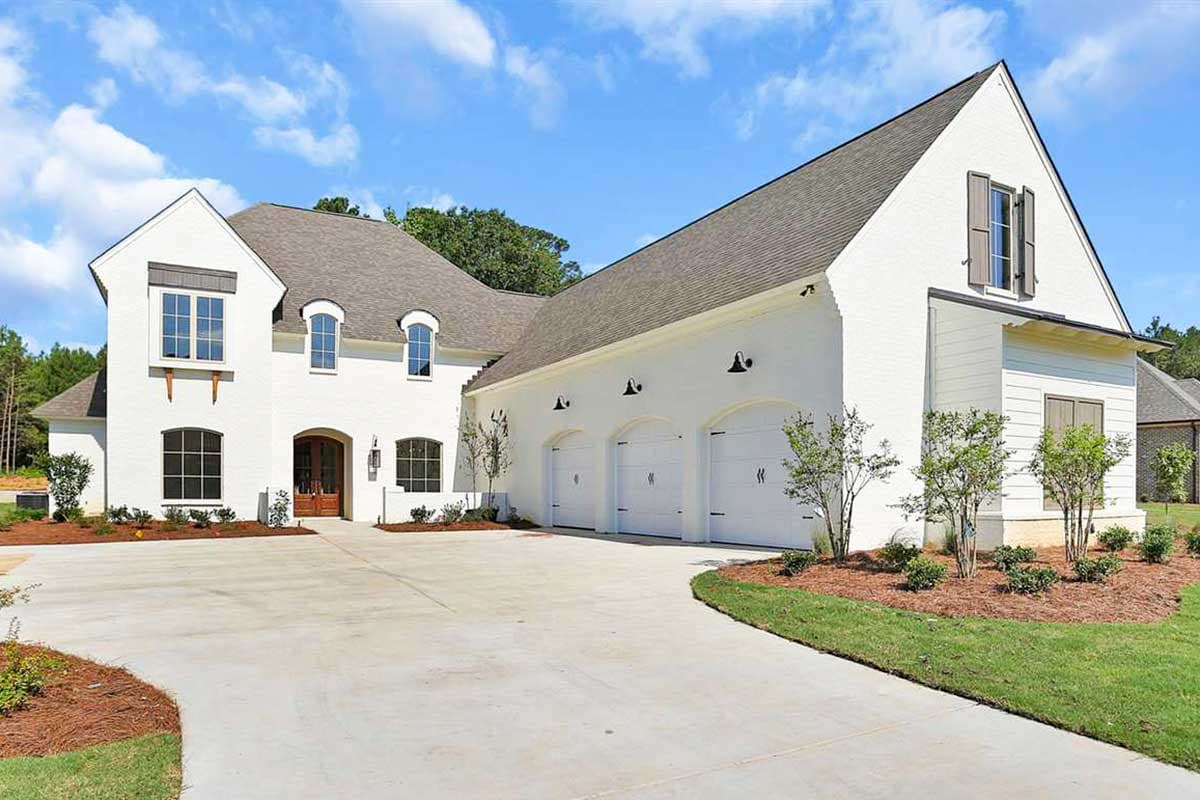 House plan exterior. Two-story with a three-car garage, gabled roof, and dormers. Features include a covered porch and brick facade.