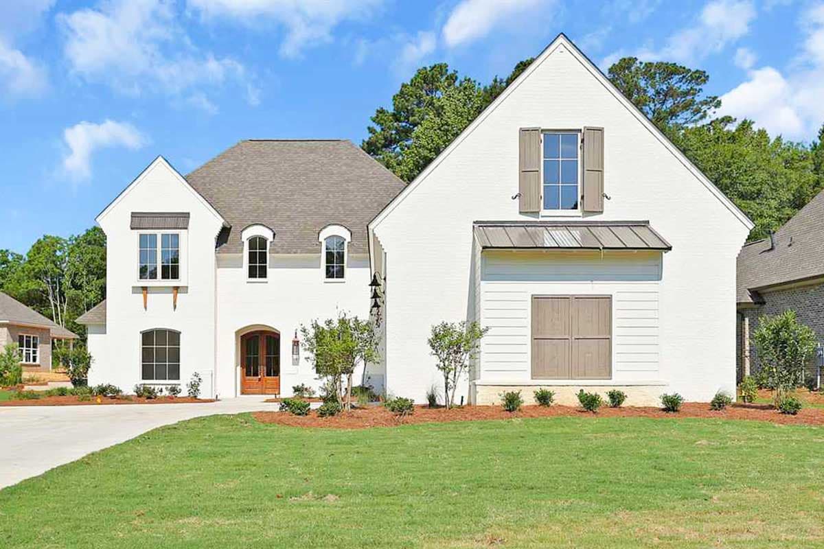 House plan exterior featuring a white brick facade, arched entry, multiple gables, and varied window styles.