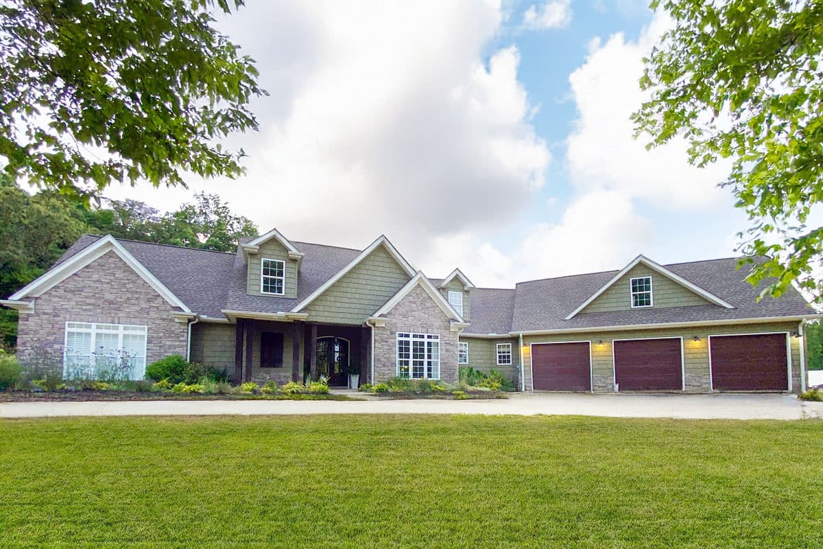 House plan exterior: Single-story home with stone accents, covered entry porch, dormers, and three-car garage.