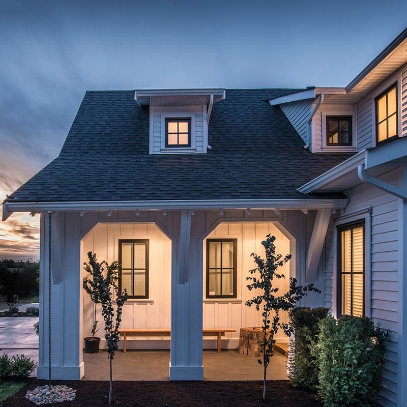 Modern farmhouse house plan exterior with gambrel roof, dormers, and covered porch with arched openings.