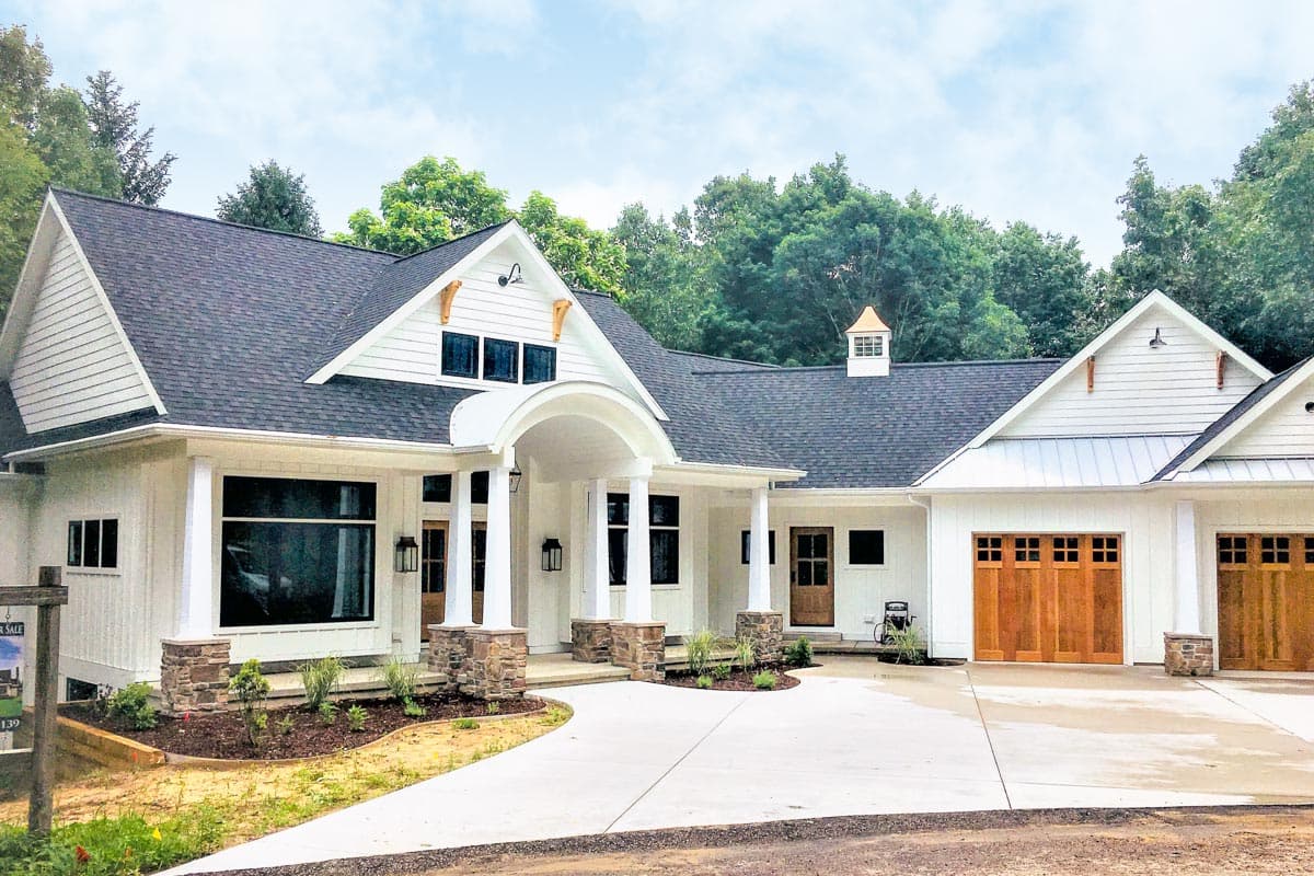 Modern farmhouse house plan exterior with a covered entry porch, stone accents, and a three-car garage with wood doors.