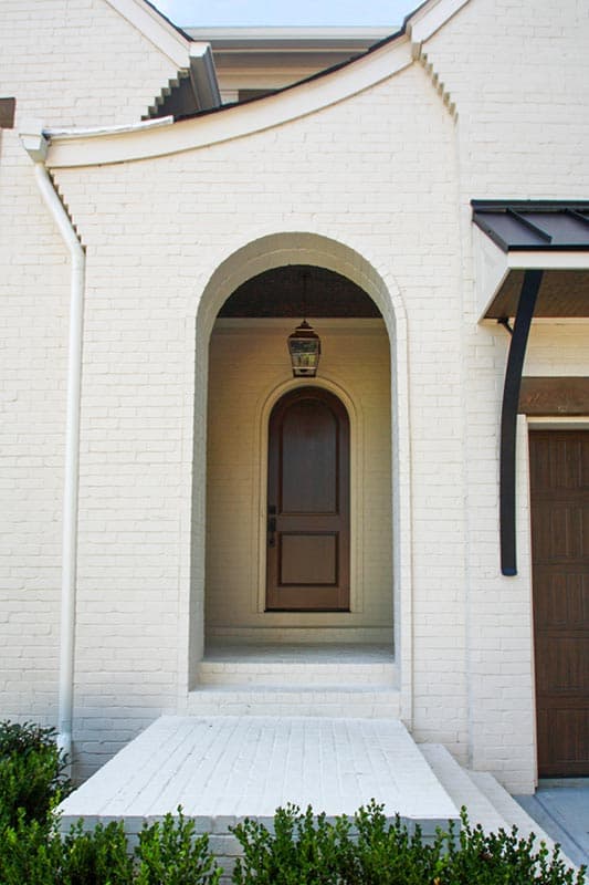 House plan exterior with arched entryway, arched wooden door, and visible rooflines.