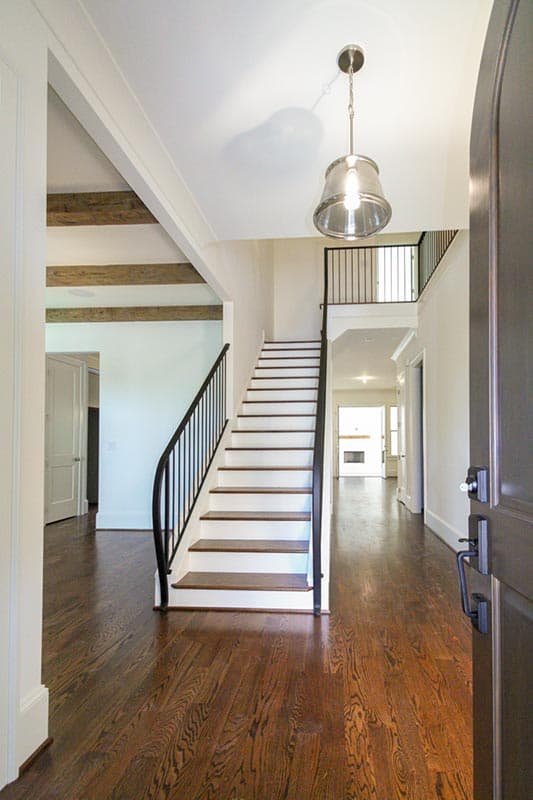 Interior view of a home entryway with a grand staircase, exposed beams, and hardwood floors.