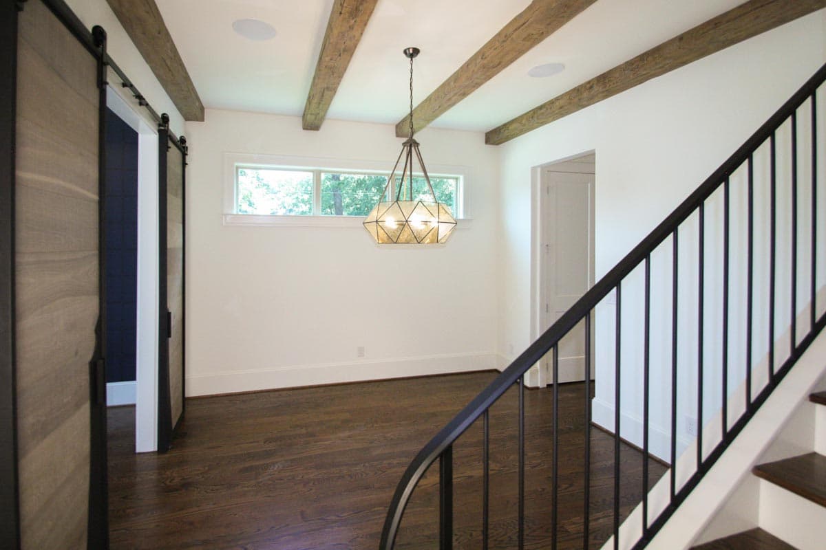 Interior view showing a room with exposed wooden beams, sliding barn doors, a long window, and a geometric chandelier.