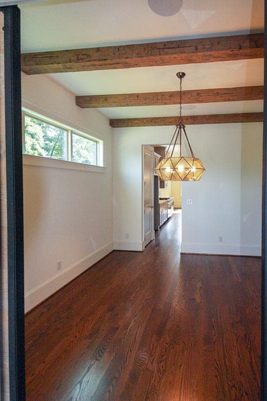 Interior view of a dining area with exposed wood beams, a linear window, and a view into the kitchen.