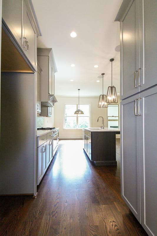Modern kitchen with gray cabinetry, dark wood island with sink, pendant lights, and a large window.