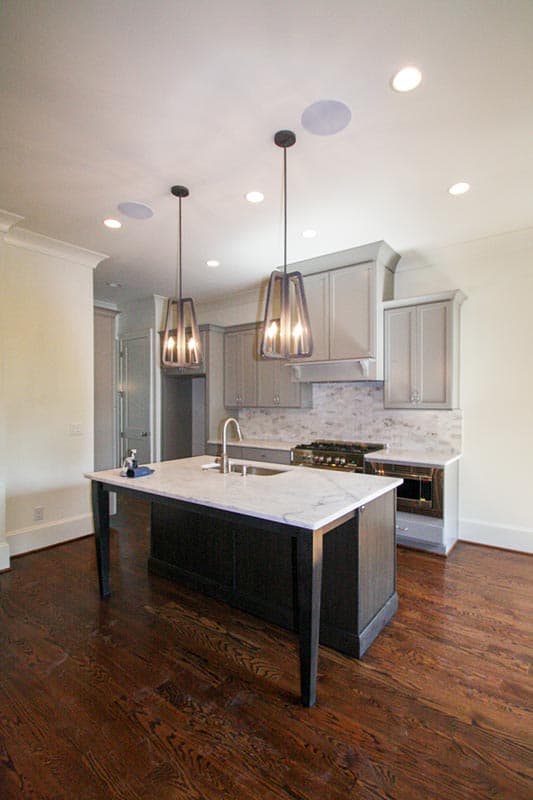 Kitchen with marble island, gray cabinets, marble backsplash, stainless steel range, and pendant lights.