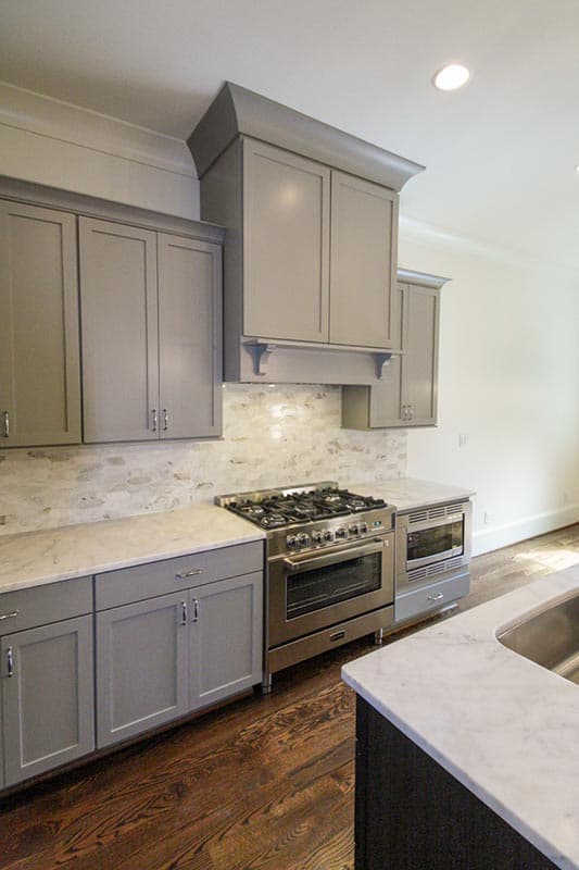 Kitchen interior with gray cabinets, stainless steel range, marble countertops, and marble backsplash.