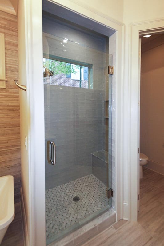 Modern bathroom with glass-enclosed shower featuring gray tile, built-in bench, and mosaic tile floor.