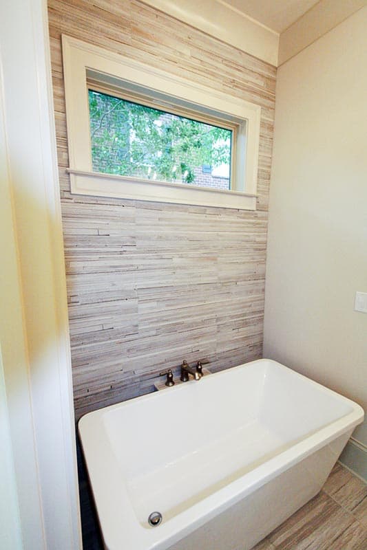 Freestanding soaking tub with horizontal plank tile accent wall and a small casement window.
