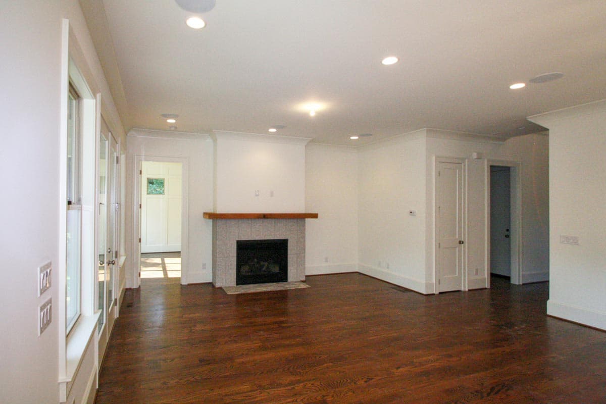 Interior view of a living area with a tiled fireplace, hardwood floors, and a wall of windows leading to an entryway.