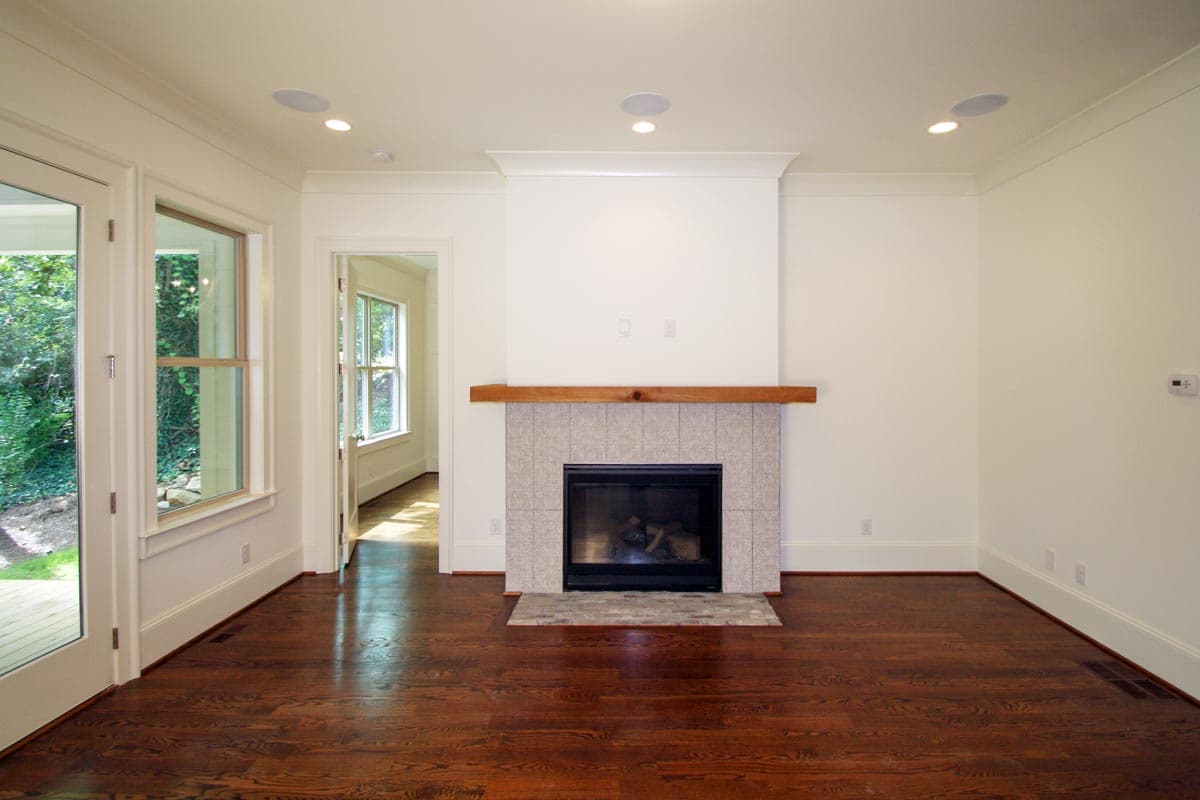 Living room with fireplace, hardwood floors, and French doors leading outside. Open doorway to another room.