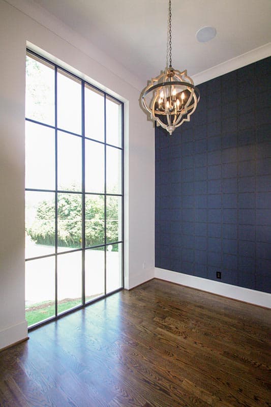 Interior view of a room with a large grid window, dark patterned wallpaper, and a geometric chandelier.