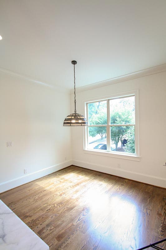 Interior view of a room with hardwood floors, a large window, and a decorative pendant light fixture.