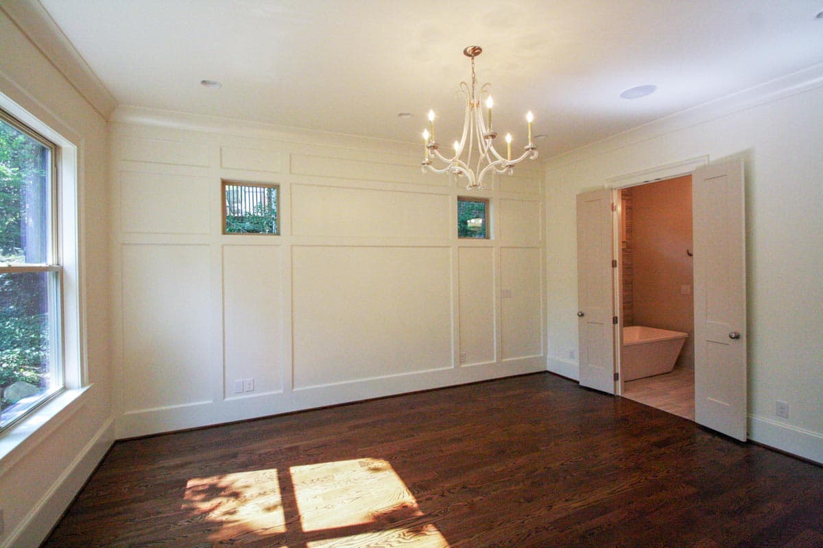 Interior view of a room with wainscoting, a chandelier, large window, and double doors opening to a bathroom with a freestanding tub.