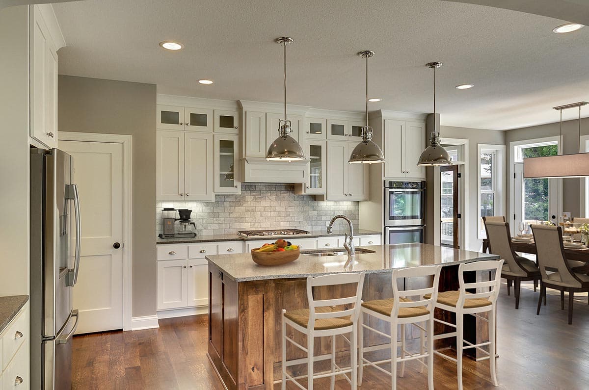 Kitchen with white shaker cabinets, granite countertops, large island with seating, subway tile backsplash, and stainless steel appliances.