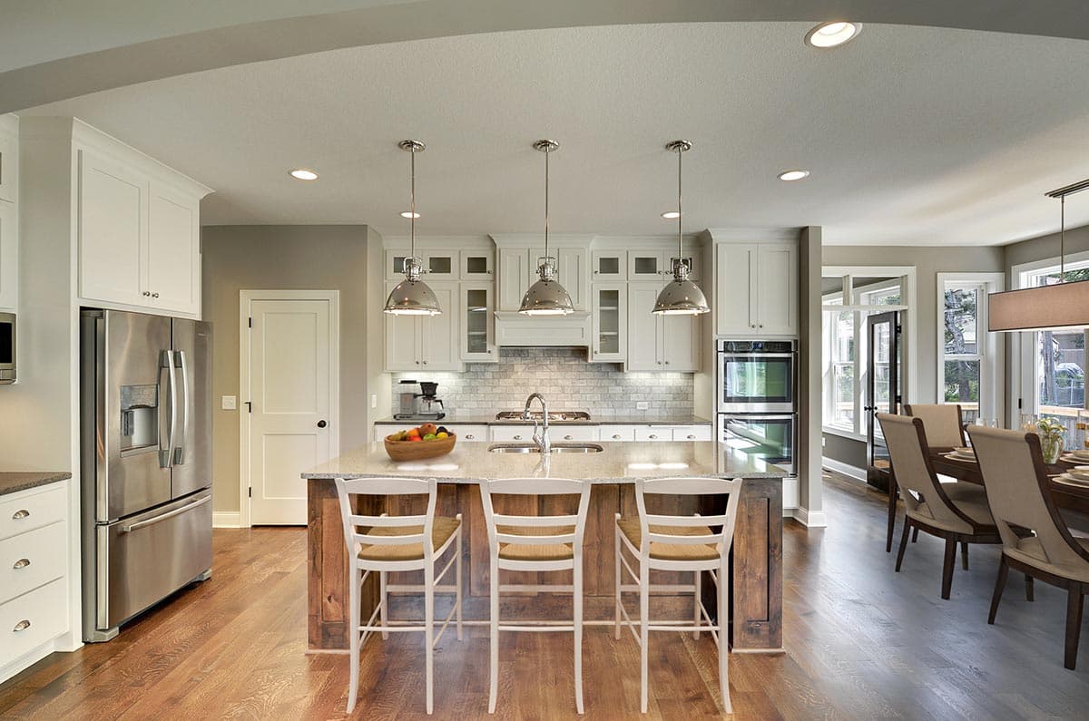 Kitchen with island, double ovens, stainless steel refrigerator, white cabinets, and adjacent dining area.